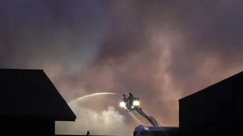Firefighter using water cannon from ladder top. Black smoke in background Stock Footage 95815061