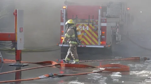 Firefighter walking in the smoke surrended by firetrucks Stock Footage 105174831