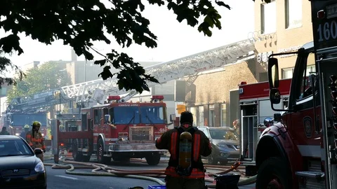 Firefighters drinking water at building fire with firetruck and ladder Stock Footage 119866714