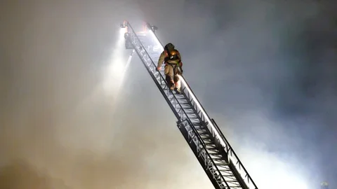 Firefighters on ladder at major structure fire Stock Footage 116012593