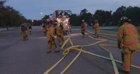 Firefighters pull a yellow fire hose along the ground to prepare it to Stock Footage 102419896