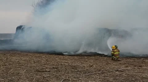 Firefighters spray round bales on fire in a field Stock Footage 12617311