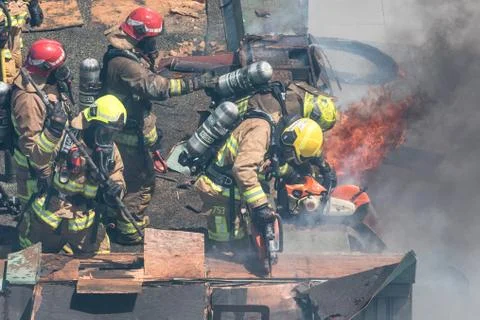 Firefighters using axe and saw for ventilation on involved roof. Stock Photos