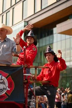 Firefighters wave while riding on a float in the Calgary Stampede Parade. The Stock Photos