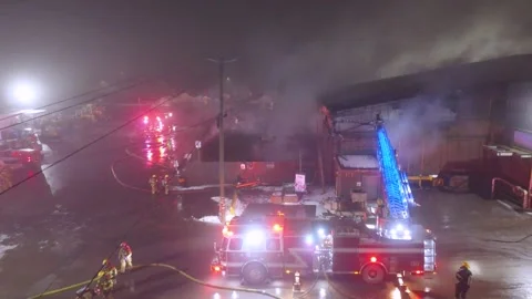 Firefighters working to contain a warehouse fire at night with heavy smoke Stock Footage 303882851