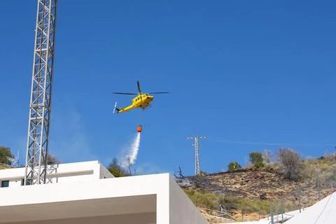 Firefighting helicopter extinguishing forest fire near residential area in Spain Fotos Stock