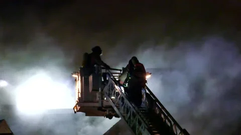 Fireman escalading ladder at night during structure fire Stock Footage 139657114