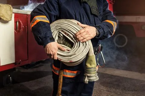 Fireman (firefighter) in action with a rolled fire hose  near a firetruck Foto stock