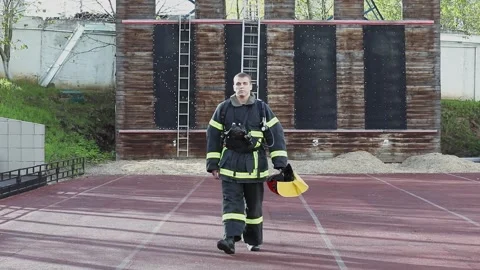 Fireman in fireproof suit puts off red helmet and walks from fire tower on Stock Footage 276368530