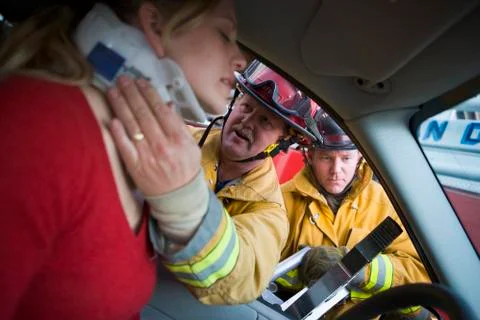Fireman helping woman with neck brace while another fireman uses the jaws of Stock Photos