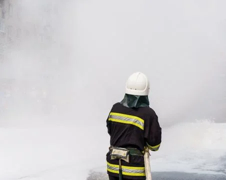 Fireman with a mask extinguishes a fire using white foam. Stockfoto's