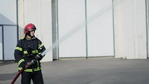 Fireman in protective uniform and helmet holds hose which spraying high pressure Stock Footage 276368508