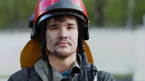 Fireman in red fire helmet looks around and smiles with soot on face. Slow Stock Footage 276368555