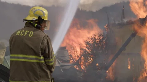 Fireman shoots a powerful stream of water onto a raging structure fire Stock Footage 59222140