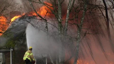 Fireman spraying water on a building consumed by fire Stockbeeldmateriaal 12547529