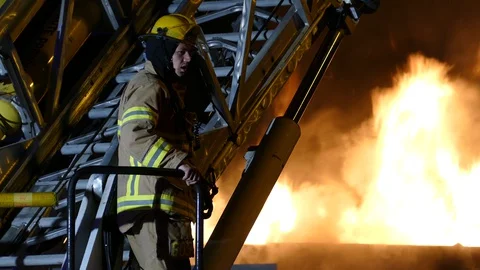 Fireman standing in foreground of intense heavy flames in background Stock Footage 129987900