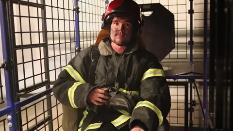 Fireman wearing protective suit and helmet sits among smoke in cage of training Stock Footage 276368572