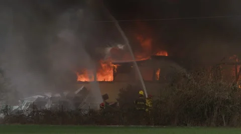 Firemen aim hoses to rain down water onto a house engulfed in flames Stock Footage 59221462