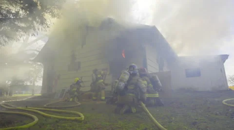 Firemen crouch outside a burning house Stock Footage 60753055