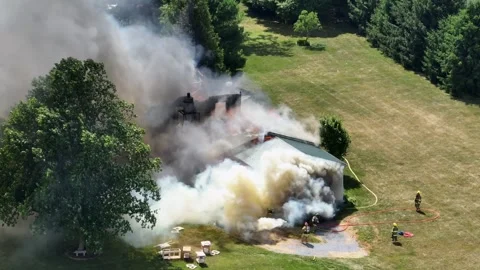 Firemen in protection clothes spraying water with hose on burning house in Stock Footage 280101377