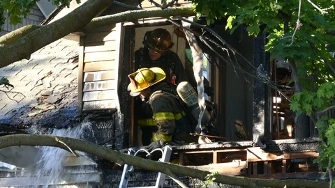 Firemen putting out rest of a fire from a second story opening of damaged house Stock Footage 94860778