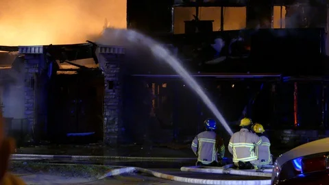 Firemen sitting in front of darken damaged building walls during fire Stock Footage 129987620