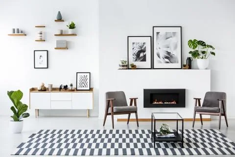 Fireplace between grey armchairs in modern living room interior with posters. Stock-Fotos