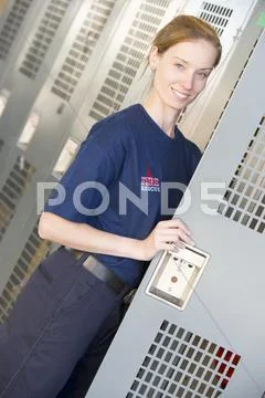 Firewoman holding her locker door open in fire station locker room (depth of Stock Photos