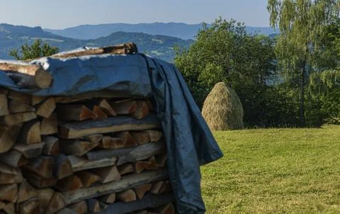 Firewood stack covered with tarp in a mountain countryside during summer Stock Photos
