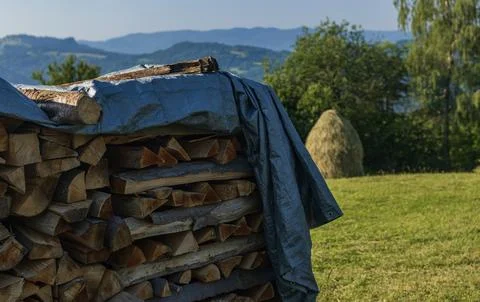 Firewood stack covered with tarp in a mountain countryside during summer Photos