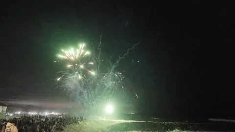A fireworks display explodes in the night sky above a crowd gathered on a beach Stock Footage 344829827