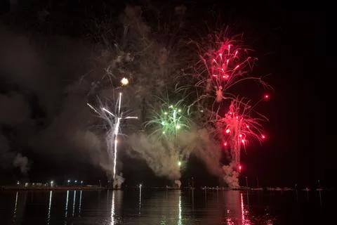 Fireworks explode above calm water at night Stock Photos