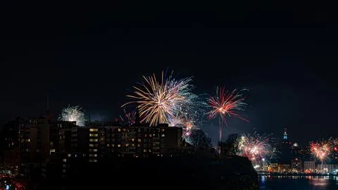 Fireworks explode in the night sky above city buildings at night Stock Photos