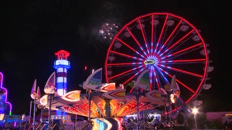 Fireworks explode in the night sky behind a ferris wheel at a carnival or state 库存影片 41983551