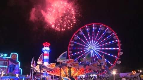 Fireworks explode in the night sky behind a ferris wheel at a carnival or state Stock Footage 41983867