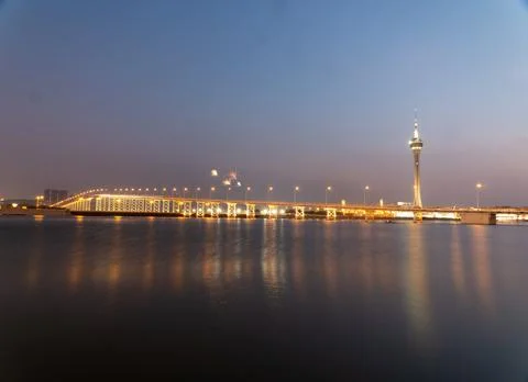 Fireworks explode over illuminated bridge and tower at dusk. Stock Photos