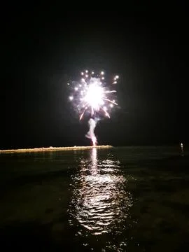 Fireworks exploding over calm water at night, bright burst of light reflecting Fotos Stock