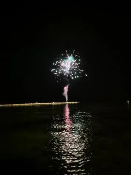 Fireworks exploding over calm water at night, colorful burst of light reflected Fotos Stock