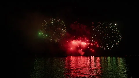 Fireworks exploding over dark water at night, creating light and smoke, with a Stock Footage 343282430