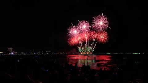 Fireworks Exploding Over Ocean Waters With Crowd Silhouettes On Beach Long .. Stock Photos