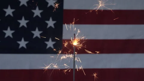 A fireworks sparkler in front of an American flag for the 4th of July Stock Footage