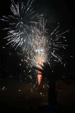 Fireworkss exploding over a black background and a small person sitting on a 写真素材