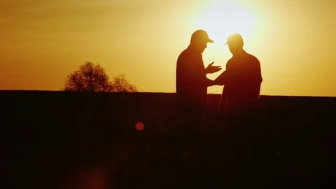 A firm handshake of two farmers on the field. They communicate, use a tablet. At Stock Footage 75381407