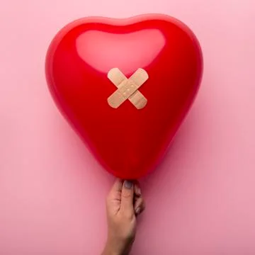 First aid with patch to wounded heart in woman hand on pink Fotos de archivo