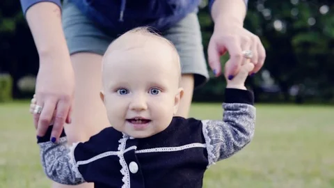 First baby's steps on the grass, mother is holding little girl's hands Stock Footage 77634915