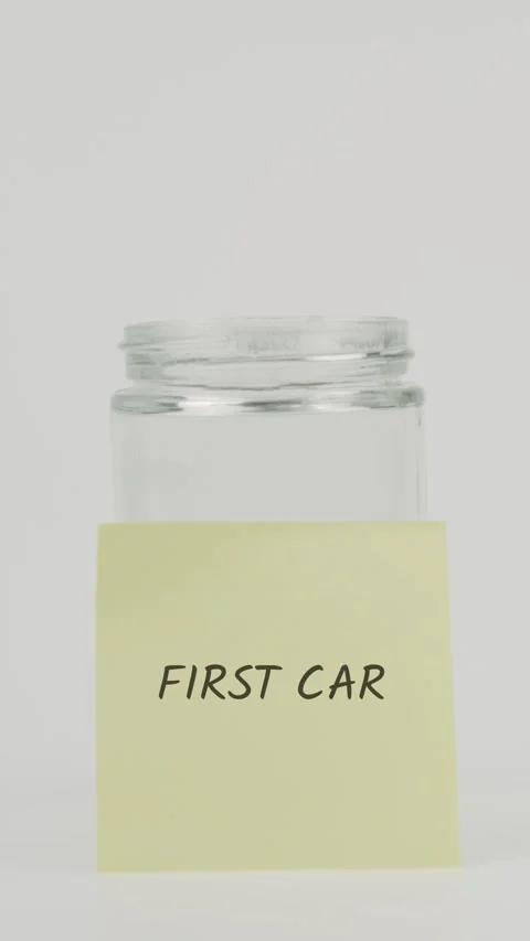 First Car text or word on yellow sticky note attached to glass jar with hand Stock Footage 311733991