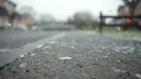 First flakes of snow fall onto pavement in slow motion during UK winter. Stock Footage 145921593
