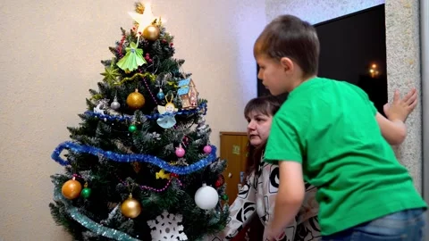 A first-grade boy and his mother decorate an artificial Christmas tree at home Stock Footage 323702044