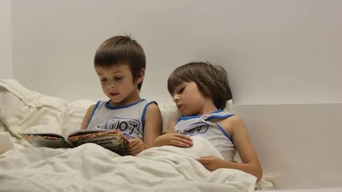 First grade boy, reading a bedtime story book to his younger brother Video stock 77651380