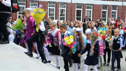 First grade pupils are entering the school in pairs holding flowers Stock Footage 106094425